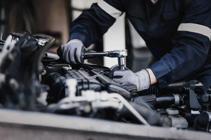 A mechanic works diligently on a car engine, using various tools to ensure proper functionality.