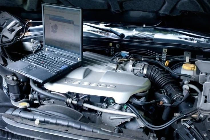 A laptop computer is located on the hood of a car, representing a fusion of modern technology and automotive aesthetics.